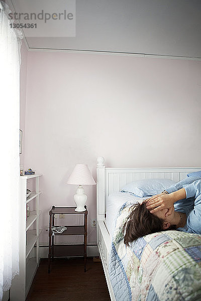 Frau bedeckt Gesicht mit Händen  während sie auf dem Bett liegt