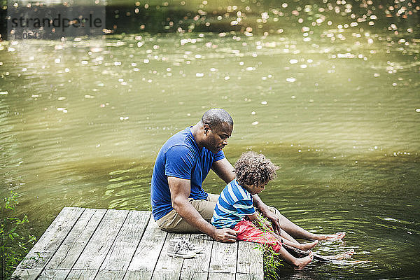 Vater und Sohn sitzen mit den Füßen auf einem Steg im See