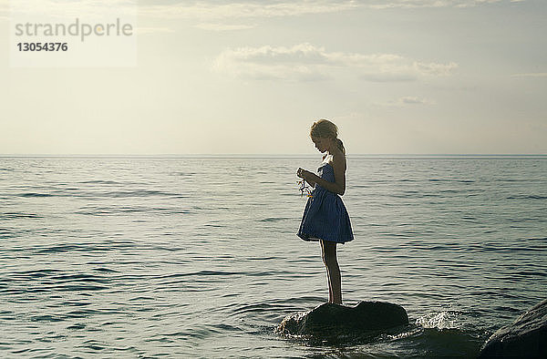 Mädchen hält Pflanze  während sie auf einem Felsen im Meer steht