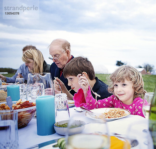 Lächelndes Mädchen isst mit Familie und Freunden am Picknicktisch