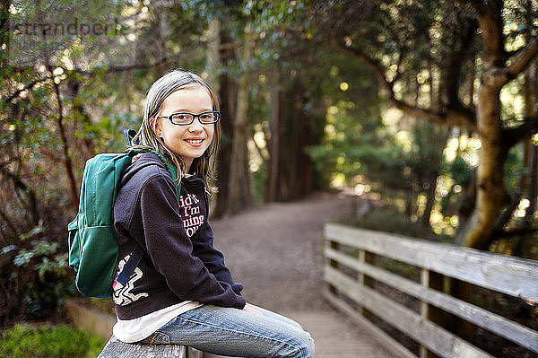 Bildnis eines Mädchens mit Rucksack auf einem Geländer sitzend