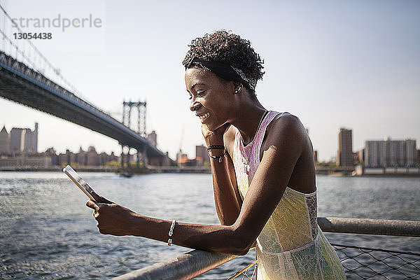 Glückliche Frau mit Tablet-Computer am Fluss mit der Manhattan Bridge im Hintergrund