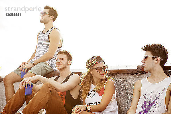 Junge Frau sitzt bei Sonnenschein mit männlichen Freunden auf der Gebäudeterrasse
