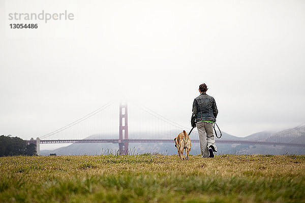Rückansicht einer Frau und eines Hundes beim Spaziergang auf dem Grasfeld im Golden Gate Park
