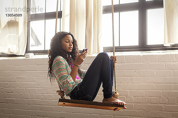 Mädchen benutzt Mobiltelefon  während sie zu Hause auf der Schaukel sitzt