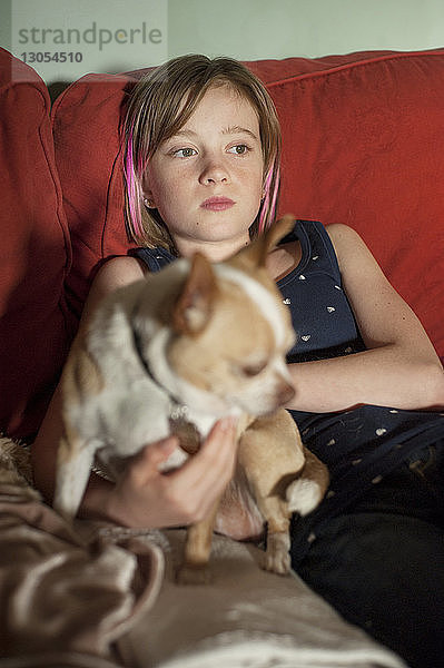 Mädchen mit Hund entspannt sich zu Hause auf dem Sofa