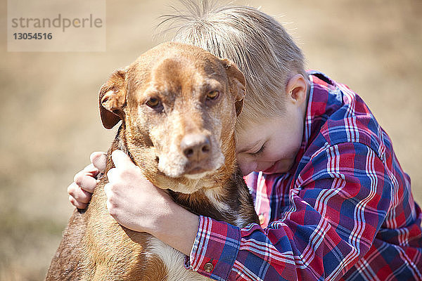 Junge umarmt Hund auf dem Feld