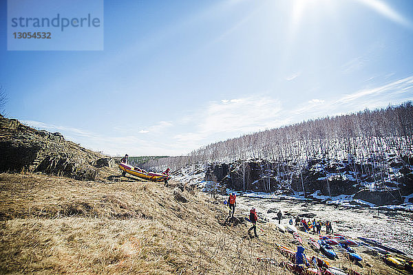 Freunde tragen an sonnigen Tagen Boote auf einem Hügel am Fluss