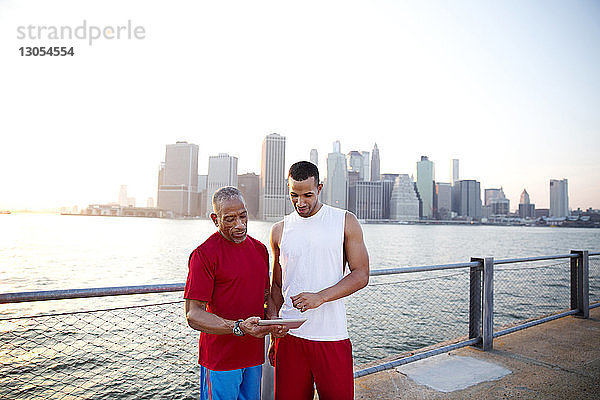 Mann und Vater benutzen einen Tablet-Computer  während sie am East River in der Stadt vor klarem Himmel stehen