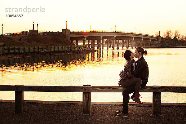 Romantisches Paar sitzt bei Sonnenuntergang auf einem Geländer gegen den Himmel