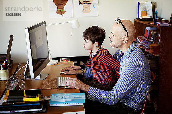 Vater und Sohn benutzen Desktop-Computer  während sie am Tisch sitzen
