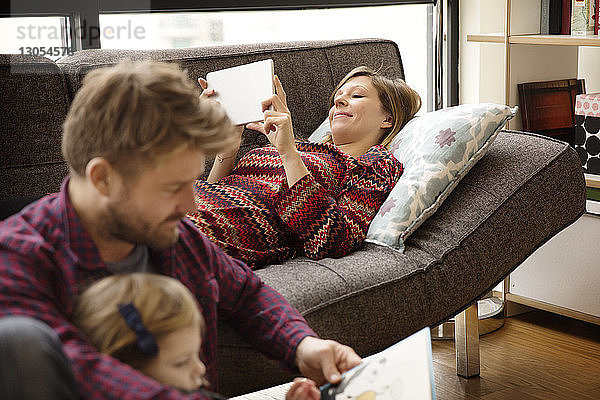 Vater und Tochter lesen ein Buch von einer Frau am Tablet-Computer  während sie sich auf der Couch entspannen