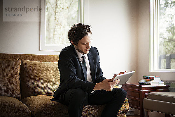 Geschäftsmann benutzt Tablet-Computer  während er zu Hause auf dem Sofa sitzt