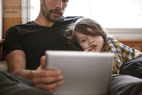 Vater und Sohn benutzen Tablet-Computer  während sie sich zu Hause im Bett entspannen