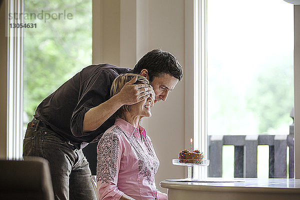 Mann bedeckt Frau die Augen  während er zu Hause Geburtstag feiert