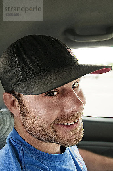 Porträt eines lächelnden Mannes mit Mütze  der im Auto unterwegs ist