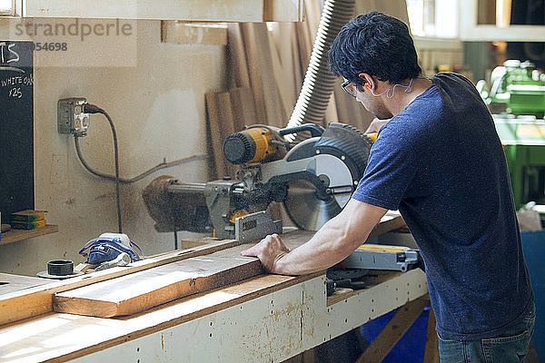 Seitenansicht eines männlichen Zimmermanns beim Schneiden von Holzbrettern mit der Elektrosäge