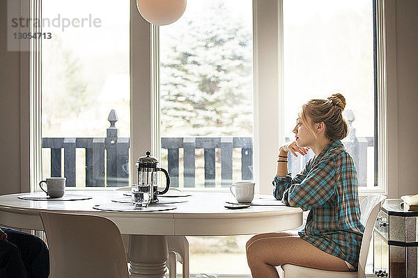 Seitenansicht einer Frau  die morgens zu Hause am Frühstückstisch sitzt
