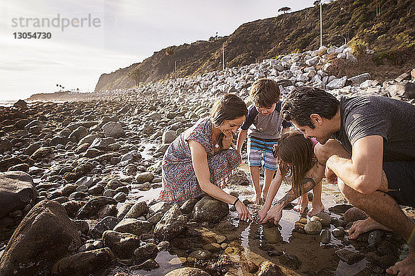 Familie taucht Finger bei Sonnenuntergang am Strand ins Wasser