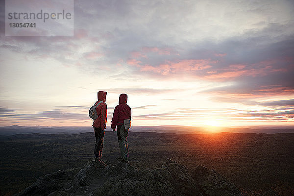 Rückansicht von Wanderern  die bei Sonnenuntergang auf einer Klippe gegen den Himmel stehen