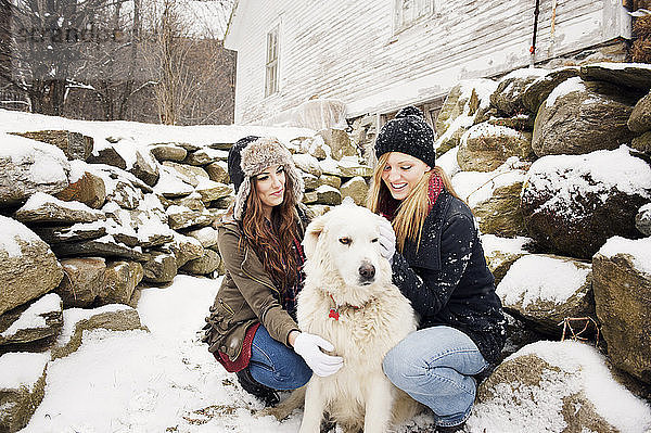 Glückliche Freundinnen mit Hund bei Steinen im Winter