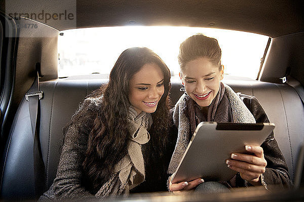 Lächelnde Freundinnen schauen auf das digitale Tablet  während sie im Auto unterwegs sind