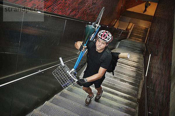 Hochwinkelansicht eines Athleten  der ein Fahrrad auf einer Rolltreppe trägt