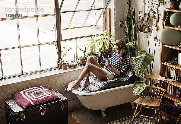 Hochwinkelansicht einer Frau  die auf einer Badewannencouch im Wohnzimmer sitzt
