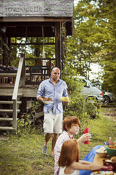 Vater hält Teller mit Kindern  die am Picknicktisch sitzen  im Vordergrund