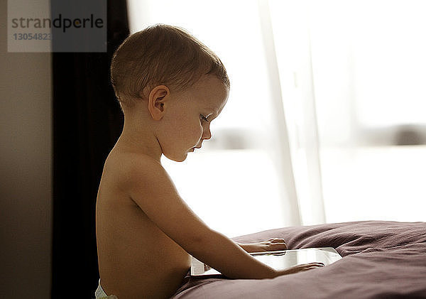 Seitenansicht eines Jungen  der zu Hause am Bett einen Tablet-Computer benutzt