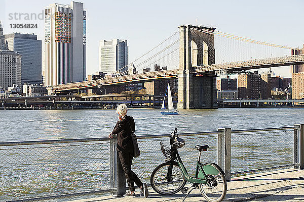 Frau schaut auf die Brooklyn Bridge über den East River  während sie auf der Promenade steht