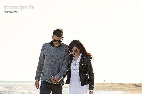 Glückliches Paar beim Strandspaziergang vor klarem Himmel