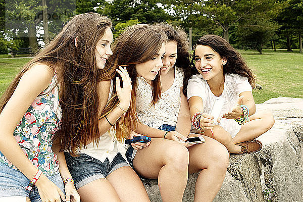 Teenager-Mädchen zeigt Freundinnen ein Handy  während sie im Park sitzen