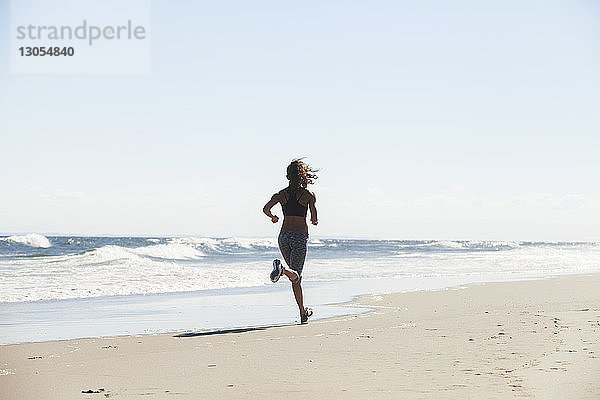 Rückansicht einer Frau  die an einem sonnigen Tag am Strand läuft