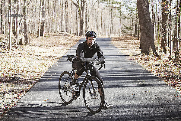 Porträt eines Radfahrers mit Fahrrad auf der Strasse im Wald stehend