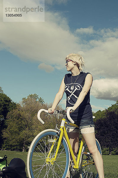 Frau steht mit Fahrrad am Park gegen den Himmel