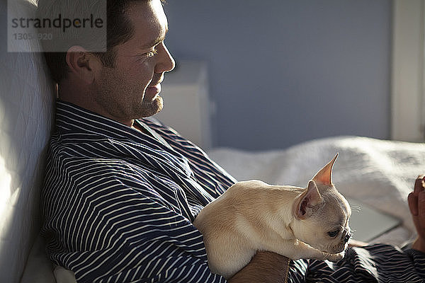 Seitenansicht eines Mannes mit französischer Bulldogge  der zu Hause auf dem Bett sitzt