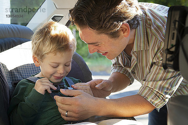 Glücklicher Vater hilft Sohn beim Anlegen des Sicherheitsgurtes