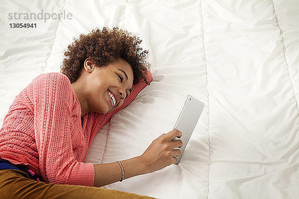 Glückliches Mädchen hält Tablet-Computer  während sie zu Hause auf dem Bett liegt