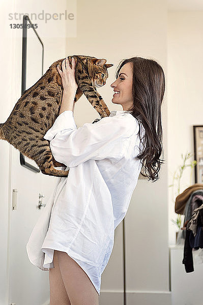 Lächelnde Frau spielt zu Hause mit Katze