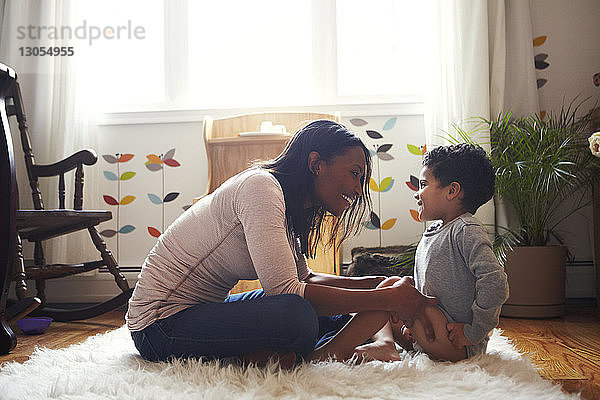 Seitenansicht einer Mutter  die mit ihrem Sohn spielt  während sie zu Hause auf dem Teppich sitzt