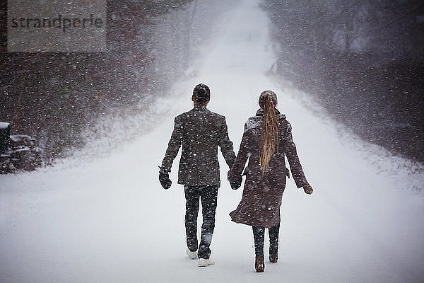 Rückansicht eines Paares  das sich beim Gehen auf einem verschneiten Feld an den Händen hält