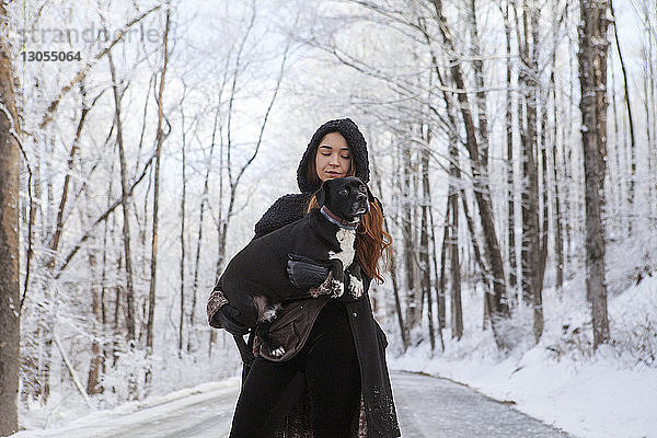 Frau trägt Hund  während sie im Winter auf der Strasse steht