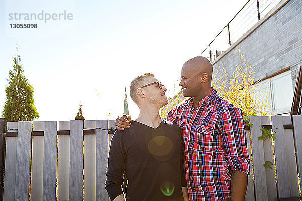 Glücklicher Mann umarmt mit seinem Freund den Arm  während er ihn an einem sonnigen Tag anschaut