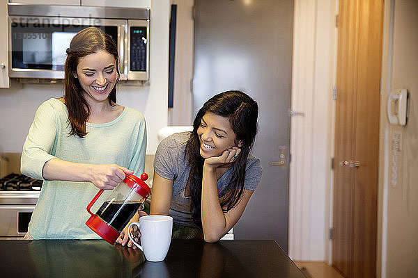 Lächelnde Frau serviert einer Freundin zu Hause Kaffee