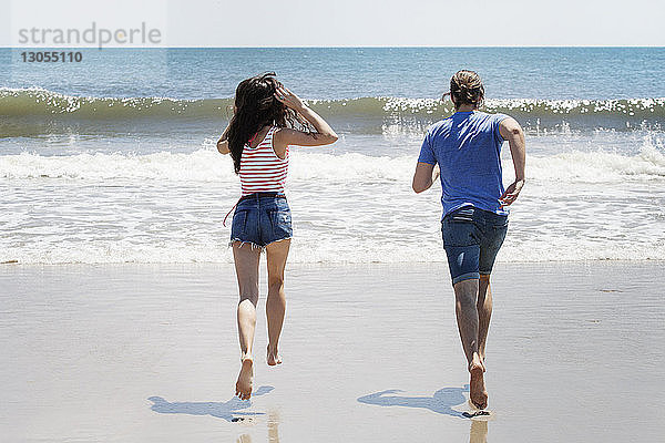 Rückansicht eines am Strand an Land laufenden Paares