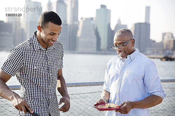 Glücklicher Mann bereitet Essen zu  während er mit seinem Vater am East River in der Stadt steht