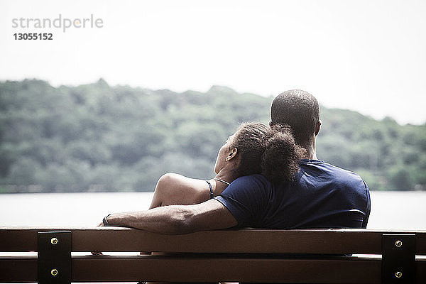 Rückansicht eines Paares  das sich bei klarem Himmel auf einer Bank entspannt