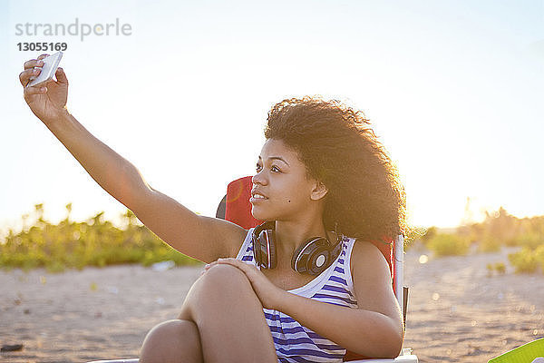 Frau  die an einem sonnigen Tag durchs Smartphone telefoniert  während sie sich am Strand entspannt