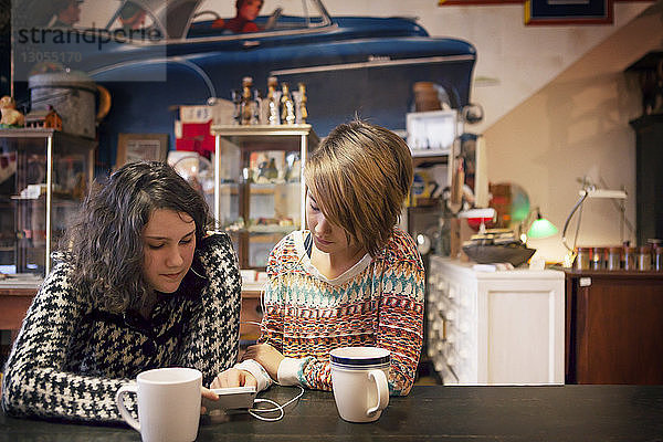 Freunde benutzen Mobiltelefon  während sie im Café sitzen